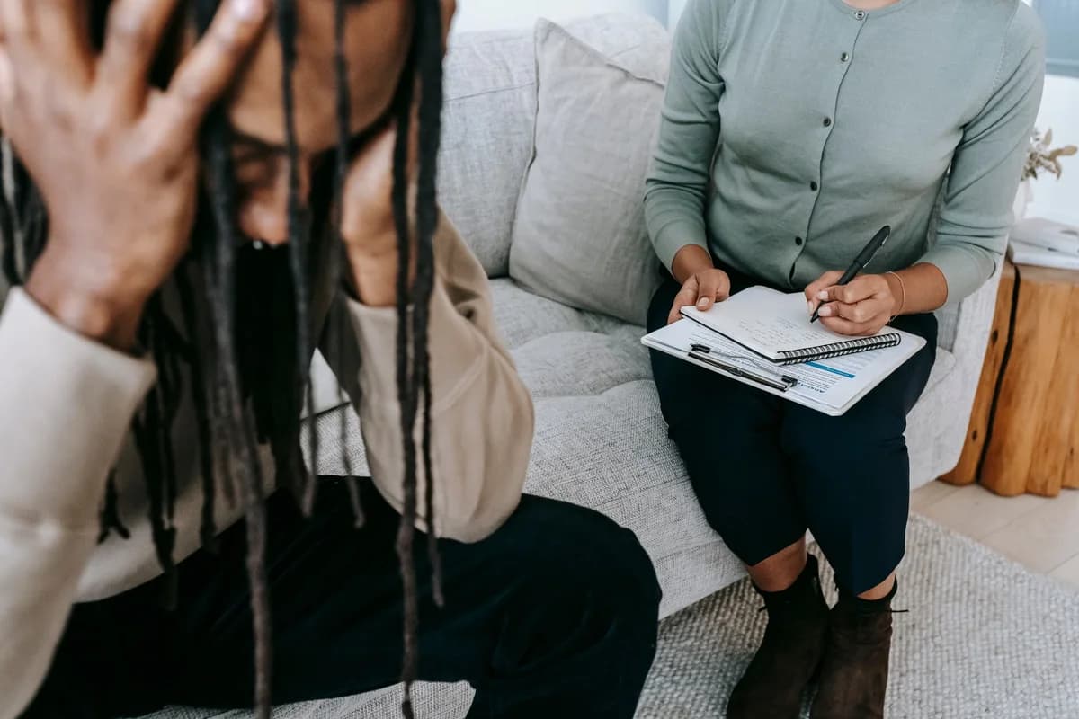 A man sits with his head in his hands while a female psychologist takes notes.