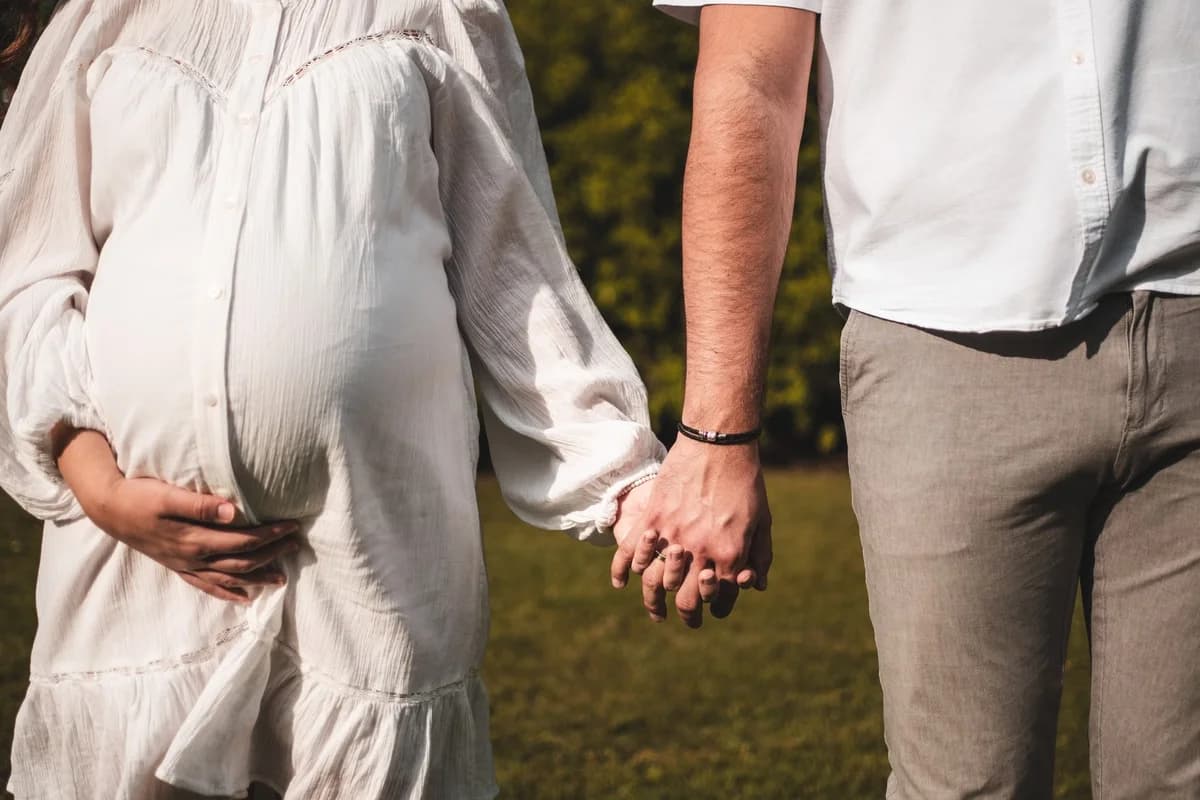 A pregnant woman and a man holding hands outdoors.