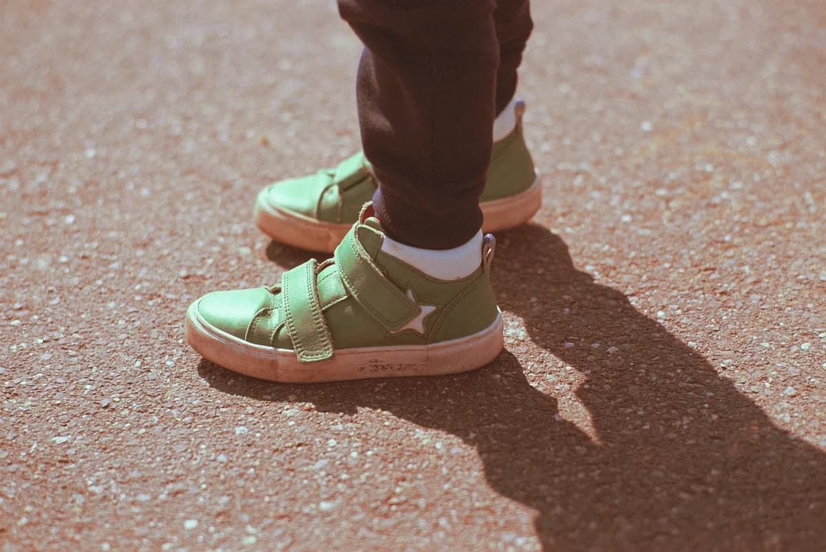Close-up of a child's green shoes on sunlit asphalt with a shadow.