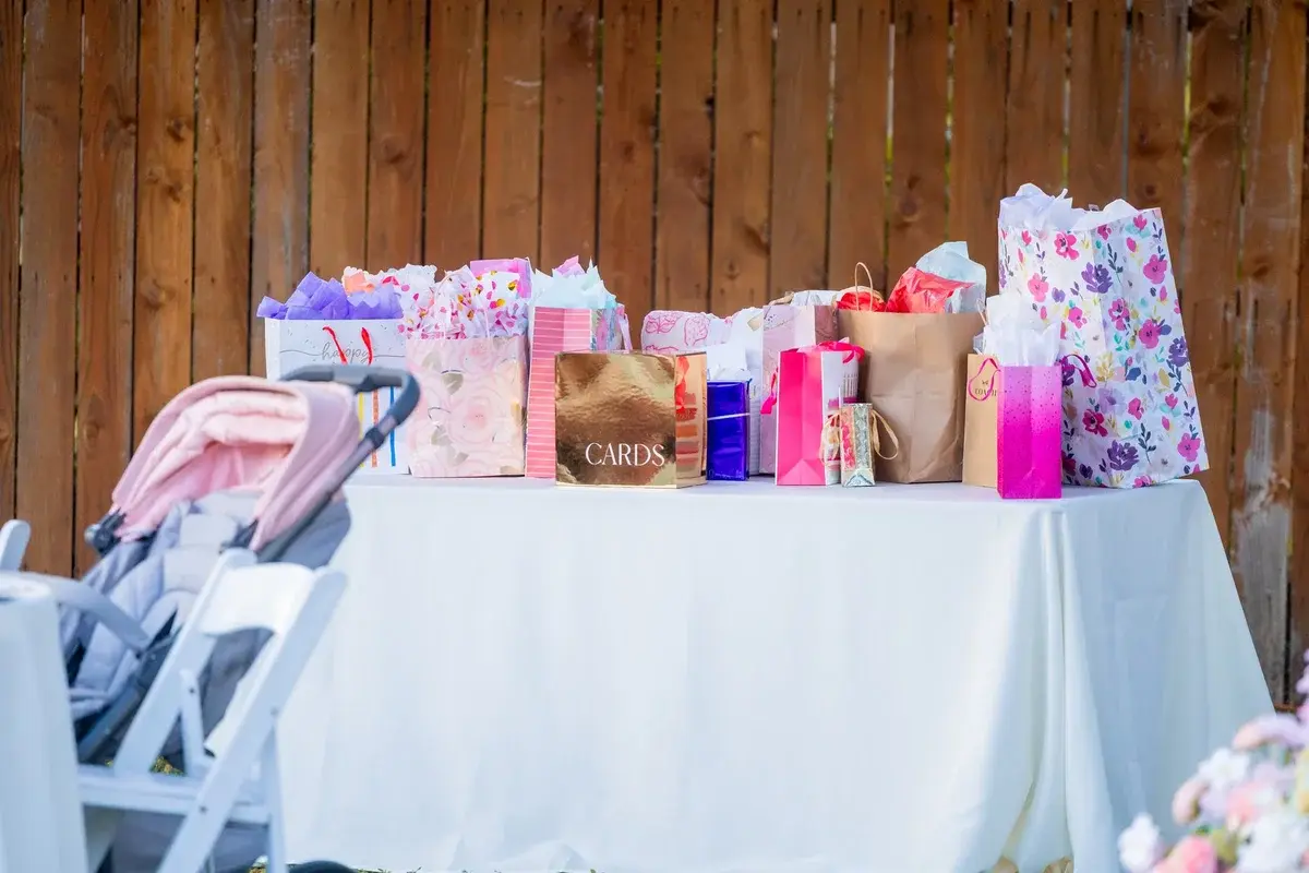 A table with colorful gift bags and a stroller at an outdoor event.