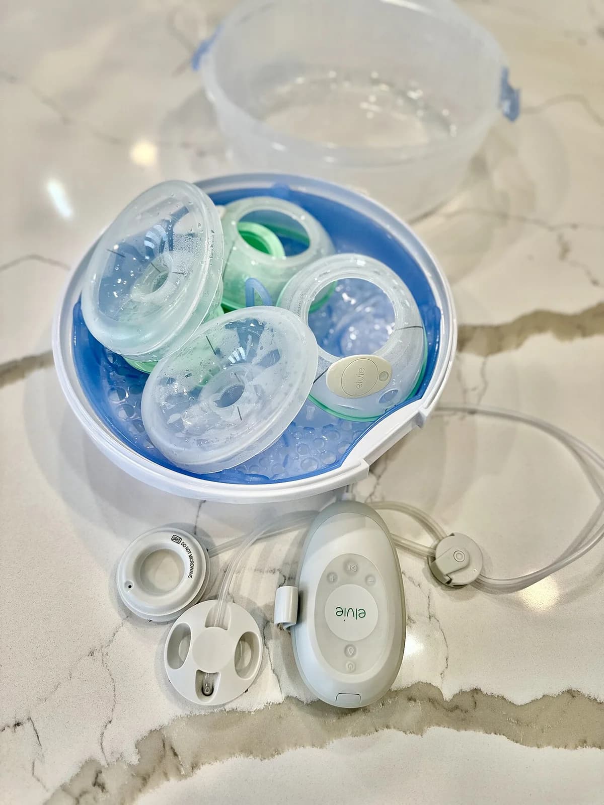Hands-free breast pump parts in a microwave sterilizer on a countertop.