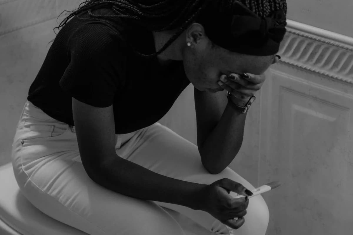 A woman in black and white looks upset while holding a pregnancy test.