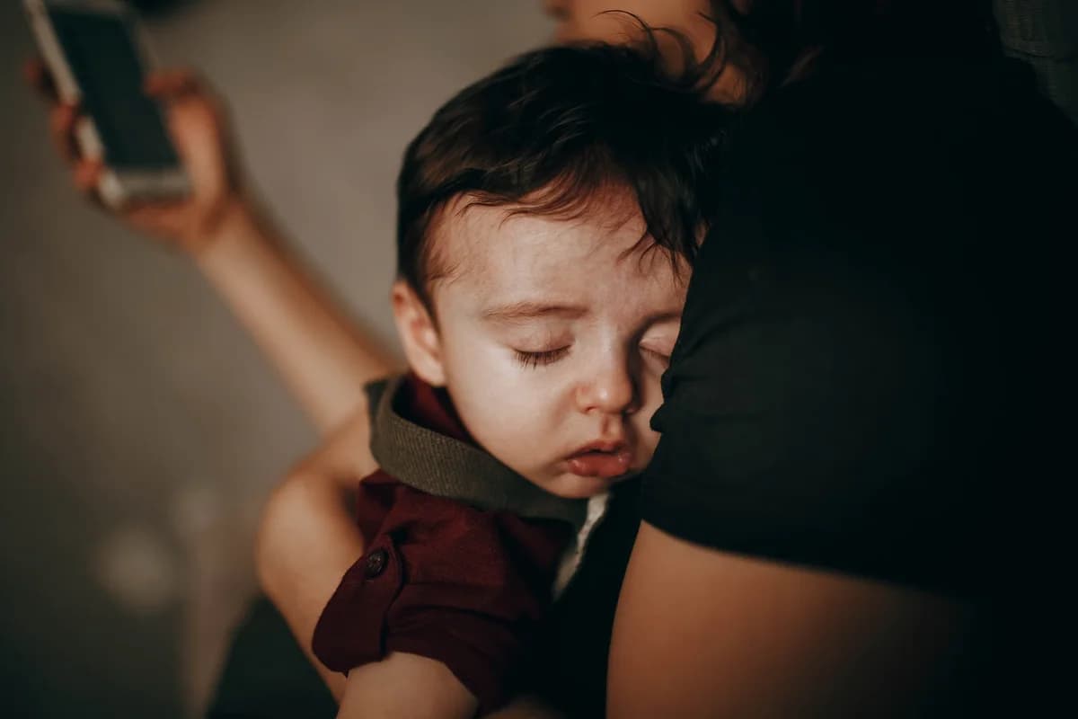 Mother holding a sleeping child while checking her smartphone.