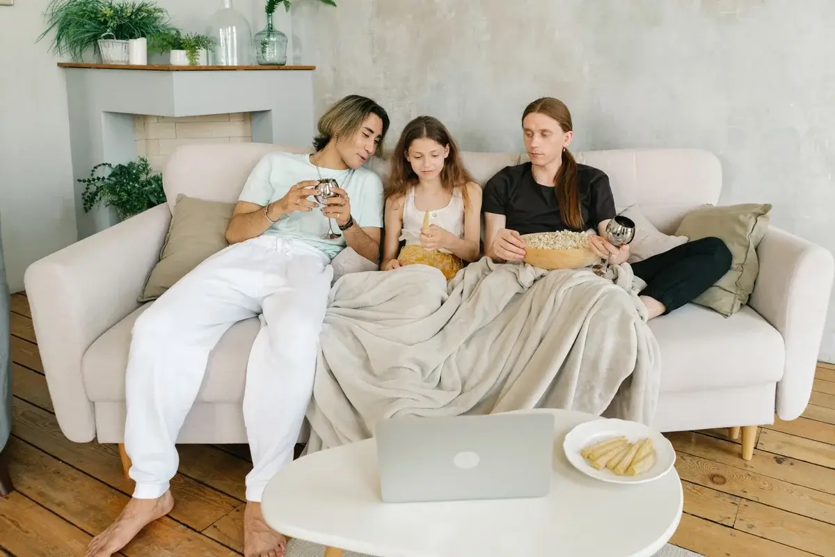 A family sitting on a couch with snacks and drinks during a movie night.