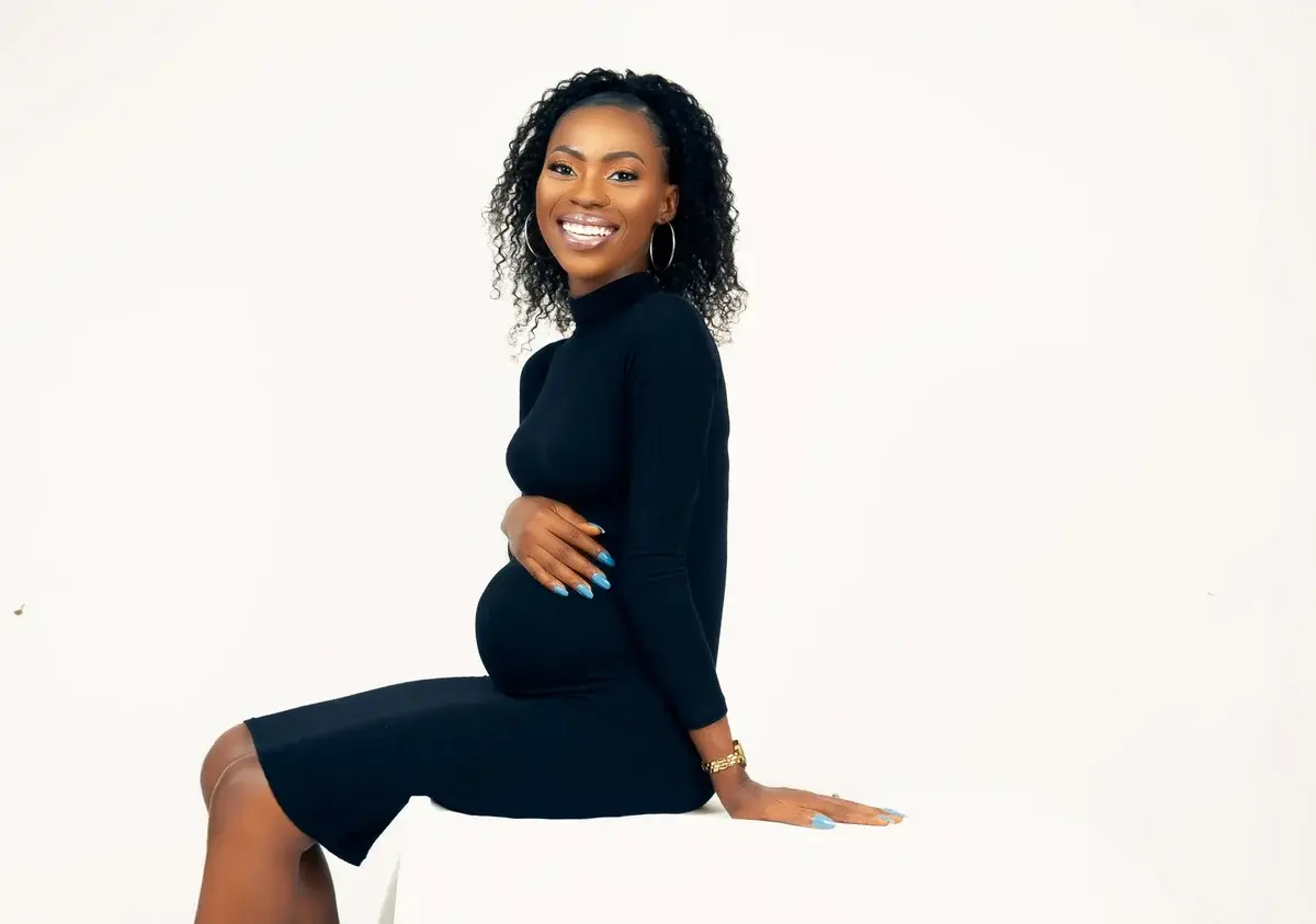A smiling pregnant woman in a black dress posing in a studio.