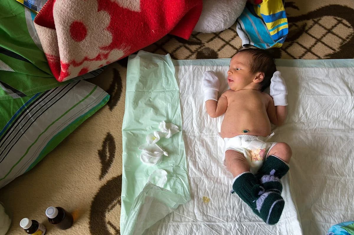 A newborn baby lying on a diaper pad on the floor.