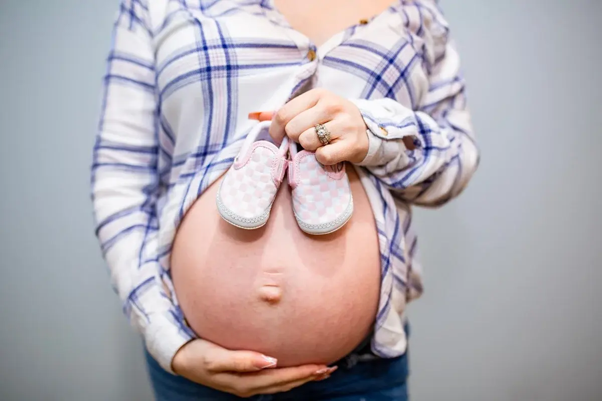 Close-up of a pregnant woman holding pink baby shoes on her belly.