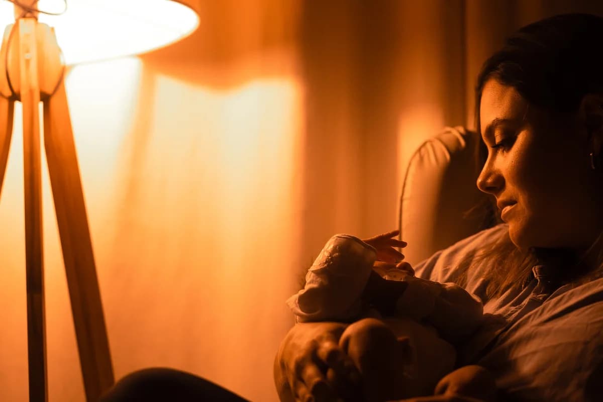 A mother gazes at her sleeping baby in warm light.