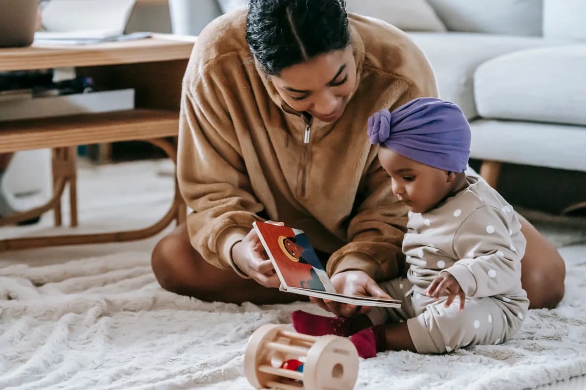 A mother reading a book to her little daughter on a rug at home.