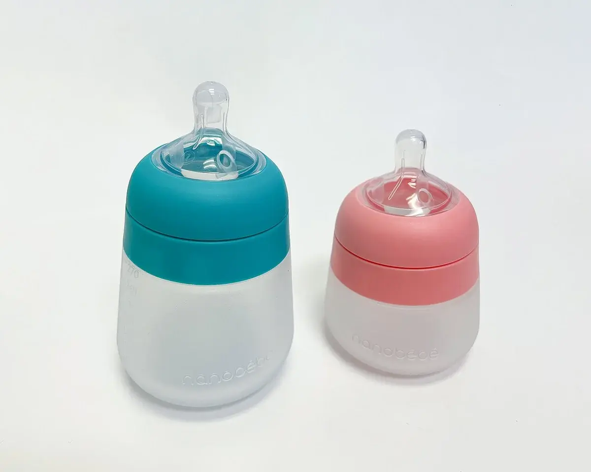Two silicone baby bottles, one teal and one pink, on a white background.