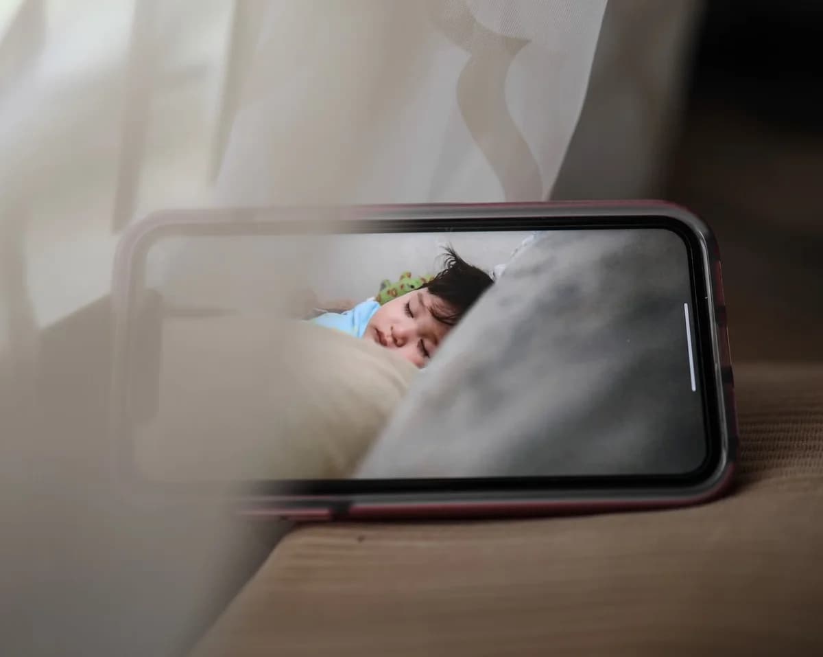 A smartphone shows a sleeping child on a baby monitor feed.