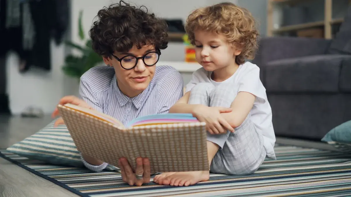 A mother and young son reading a book together on the floor.