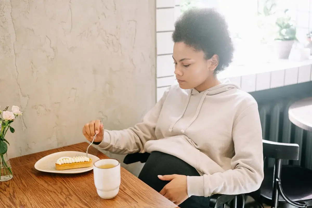 Pregnant woman eating dessert with a hot drink at a table.