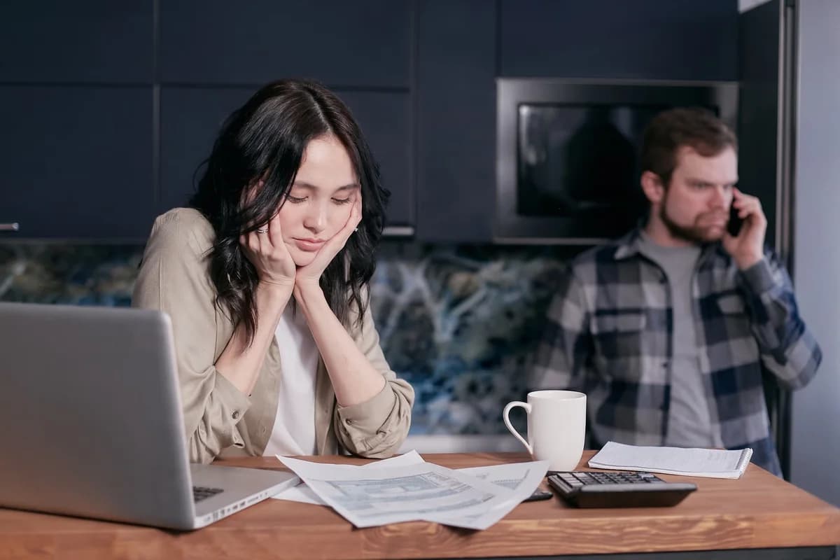 A worried couple at home with bills, a laptop, and a calculator.