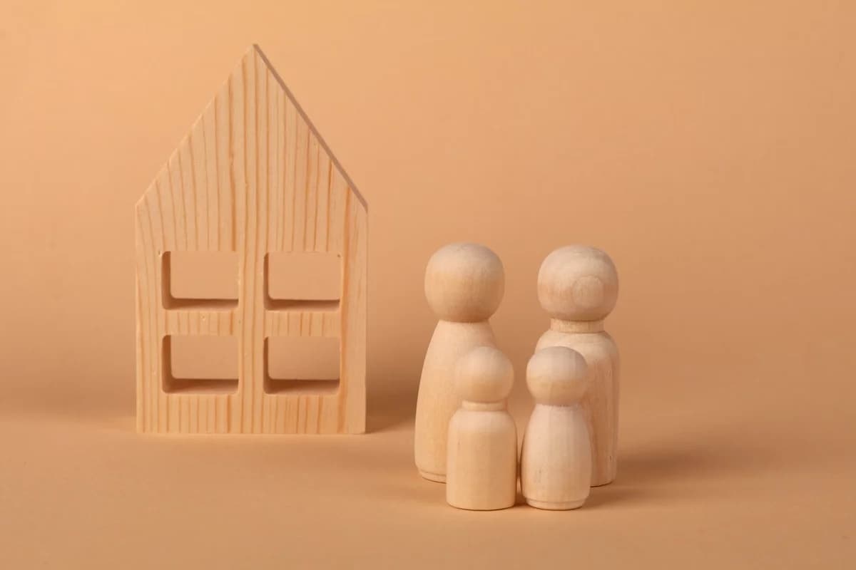 Wooden family figures next to a house model on a beige background.