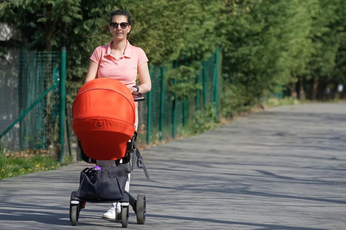 A woman pushes a stroller along a park path.